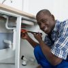 41933720-close-up-of-happy-african-male-plumber-fixing-pipe-of-sink-in-kitchen.jpg